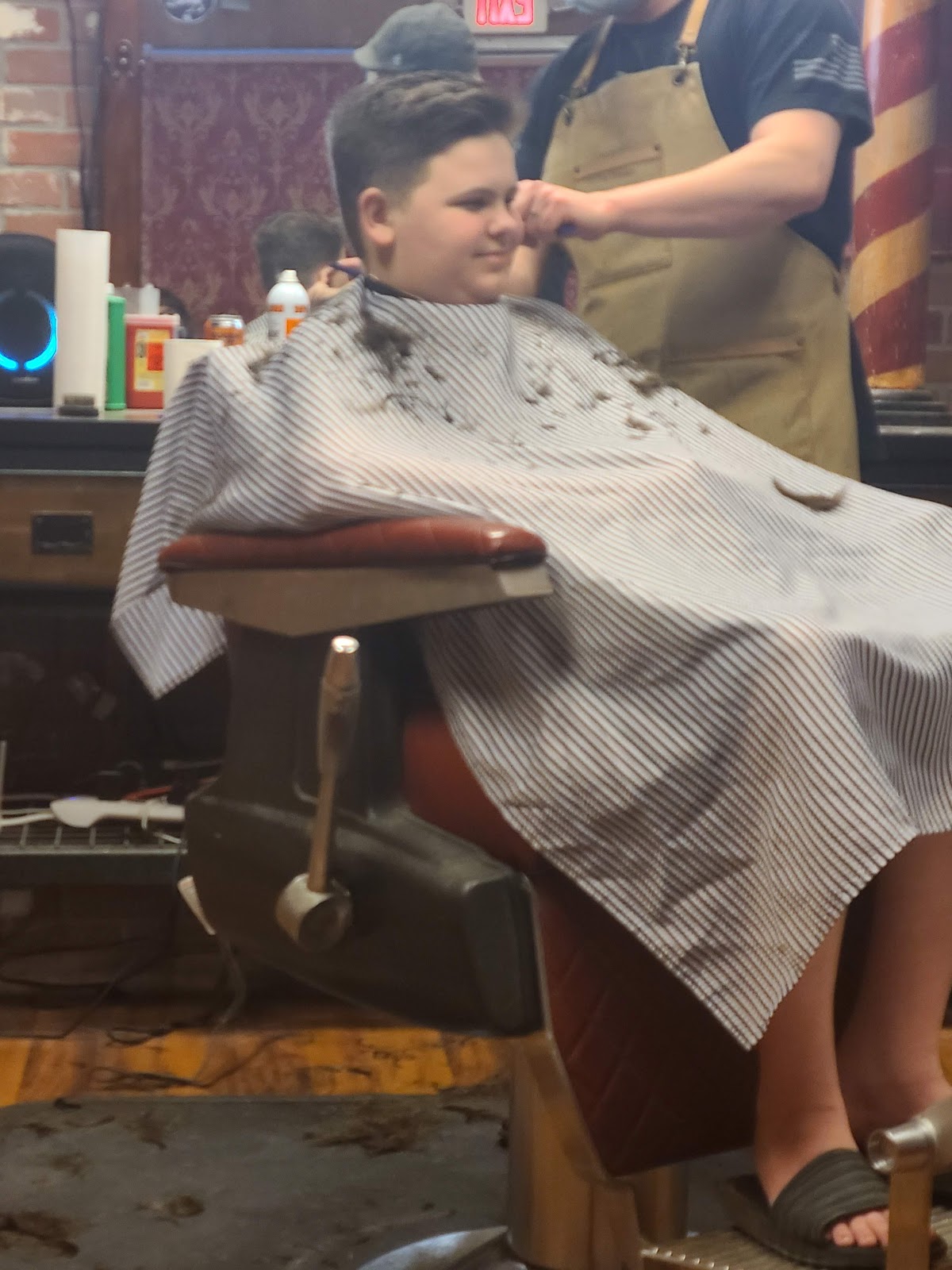 A clean cut in progress at Frasier's, American flag on the barber's sleeve